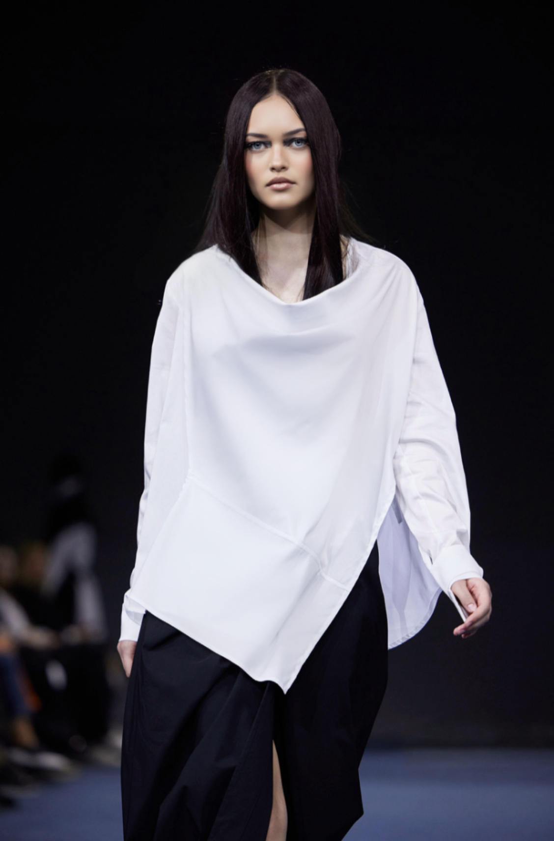 Model wearing a white oversized shirt and black pants on a runway.